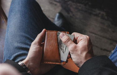 A man takes out credit cards from a brown leather wallet on a dark background, close-up, focus on...