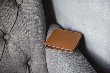 A brown leather wallet is lying on a grey textile sofa. Simplicity and elegance contrast with the...