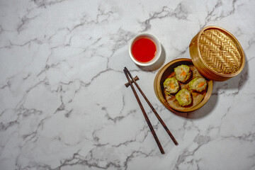 Steamed Dumpling Siew Mai served in a bamboo basket steamer with dipping sauce isolated on grey background. Flat lay.