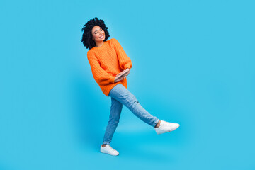 Fototapeta na wymiar Full body photo of attractive young woman cute charming pose walking wear trendy knitwear orange clothes isolated on blue color background