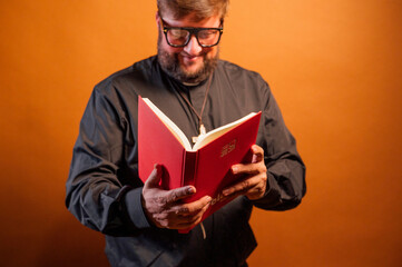 Portrait of a priest with crucifix and black shirt holding a bible.