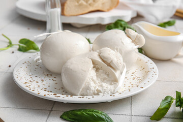 Plate of tasty Burrata cheese with basil on white tile background