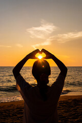 Back view of Travel asian young woman with making heart sign on sea beach at sunset in summer, Thailand.