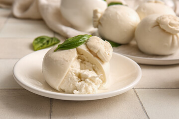 Plate of tasty Burrata cheese with basil on white tile background