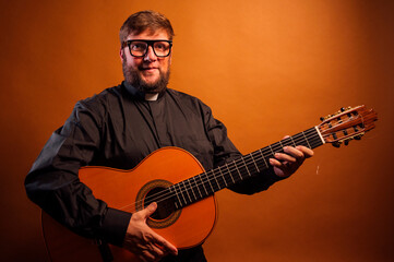 Portrait of a priest with a crucifix and black shirt playing the guitar.