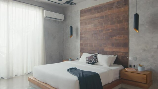 Beautiful stylish interior of bedroom with double bed with white pillows and wooden bedside tables near gray walls with air conditioning and window in hotel room of expensive guesthouse.