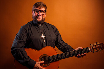 Obraz premium Portrait of a priest with a crucifix and black shirt playing the guitar.