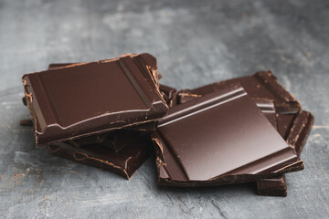 Heap of delicious dark chocolate pieces or cubes, chopped, broken chocolate bar on a dark background