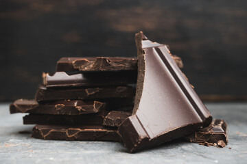 Heap of delicious dark chocolate pieces or cubes, chopped, broken chocolate bar on a dark background