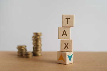 Wooden cubes with TAX word, up and down arrow with blurred stack of coins. For tax rate, percent,...