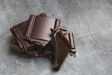 Heap of delicious dark chocolate pieces or cubes, chopped, broken chocolate bar on a dark background