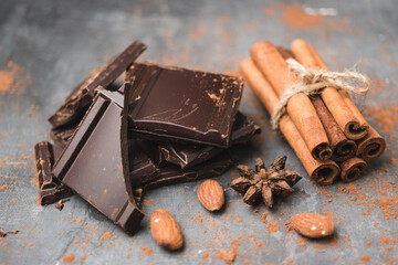Heap of delicious dark chocolate pieces or cubes, chopped, broken chocolate bar, almond nut, cinnamon sticks and star anise on a dark background