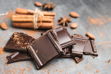 Heap of delicious dark chocolate pieces or cubes, chopped, broken chocolate bar, almond nut, cinnamon sticks and star anise on a dark background