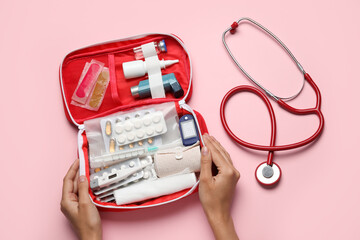 Female hands with first aid kit and pills on pink background - obrazy, fototapety, plakaty