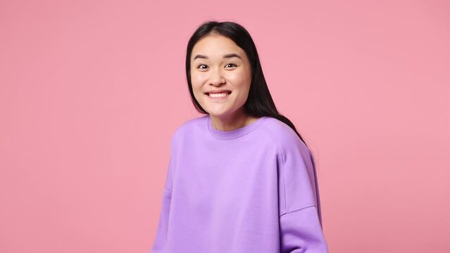 Side profile view surprised young woman of Asian ethnicity wear purple sweatshirt turn around camera spread hands say wow omg no way isolated on plain pastel light pink background. Lifestyle concept