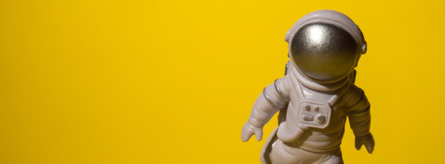 Plastic toy astronaut on colorful yellow background Copy space. Concept of out of earth travel,...