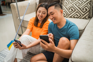 asian couple watch something on the phone after cleaning the house