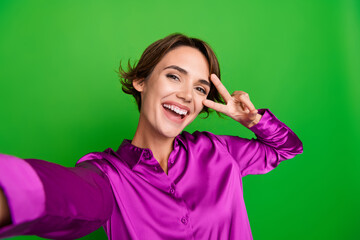 Photo of cheerful adorable funny girl dressed trendy clothes touch face v-sign video blog isolated on green color background