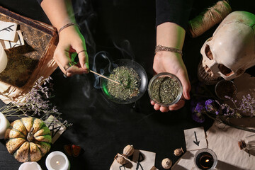 Witch burning herbs on dark table, top view