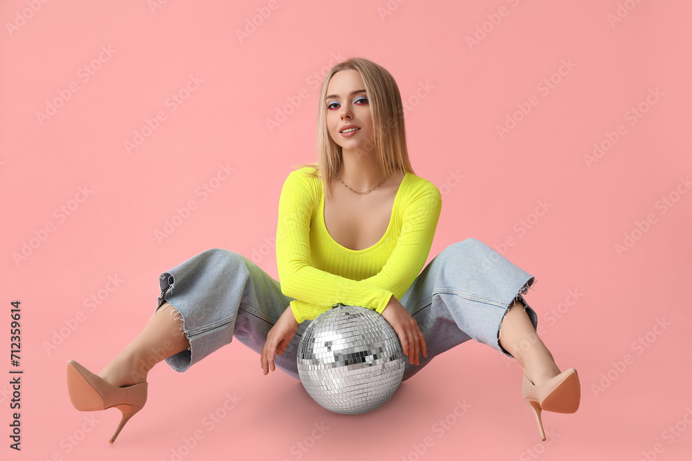 Wall mural beautiful young woman with disco ball sitting on pink background