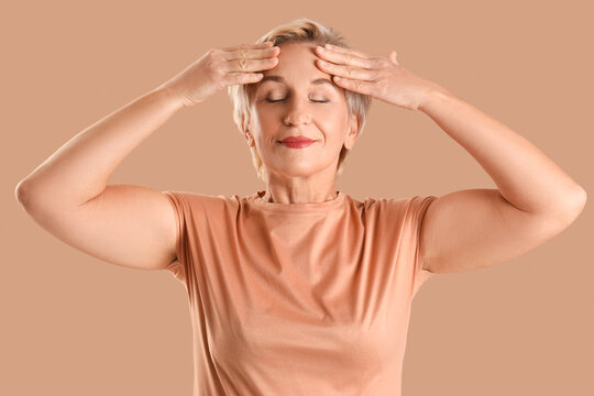 Beautiful mature woman doing face building exercise on beige background, closeup