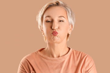 Mature woman doing face building exercise on beige background, closeup