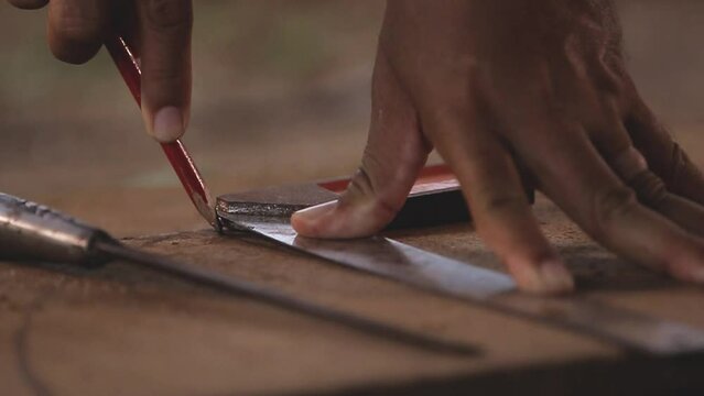 A carpenter uses a pencil to draw lines on wood to make a sketch