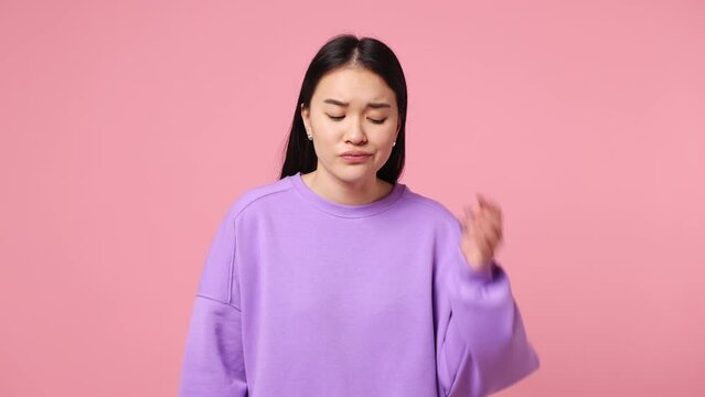 Upset pensive minded sad young woman of Asian ethnicity wear purple sweatshirt hold use mobile cell phone receive message sms and become happy isolated on plain pastel pink background studio portrait