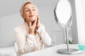Mature woman doing face building exercise near mirror in bedroom