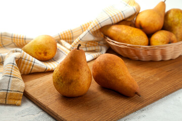 Cutting board with pears, wicker basket and yellow kitchen towel on white wooden background..