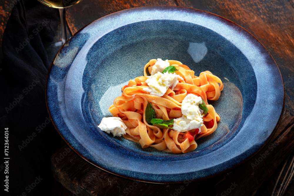 Wall mural Homemade pasta with mozzarella cheese, tomatoes and basil in a blue plate on a rustic wooden background, close up