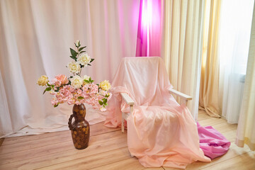 Delicate bright pink interior of the room with armchair, a vase with roses, draped curtains and a...