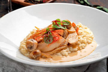 Stewed chicken with sauce, mushrooms, paprika and rice in a white plate. Risotto with chicken served on a wooden table, close up