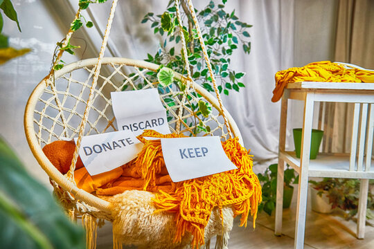 Signs with the words keep, donate, discard and fashion clothes folded in stacks in cozy room. The concept of cluttering, decluttering. Background