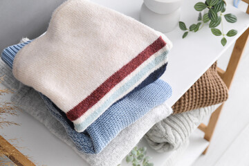 Shelving unit with stack of different stylish sweaters in room, closeup