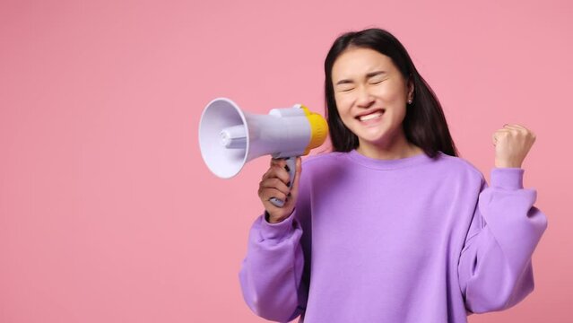 Surprised excited promoter young woman of Asian ethnicity wear purple sweatshirt scream in megaphone announces discounts sale Hurry up do winner gesture isolated on plain pastel light pink background