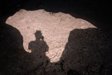 Shadow of a man on a sunny day taking a picture of his shadow while standing over the entrance to a...