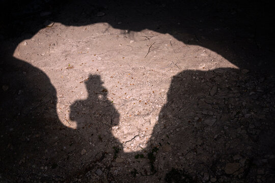 Shadow of a man on a sunny day taking a picture of his shadow while standing over the entrance to a cave.