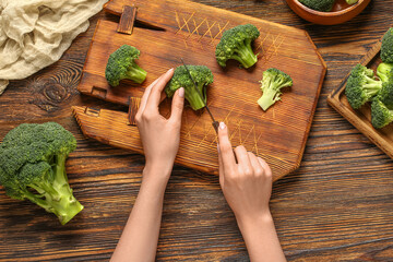 Woman cutting fresh broccoli cabbages on wooden background