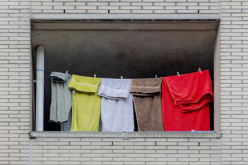 Hanging clothes on the clothesline in balcony, Drying laundry under the sun in summer, Multi color towels on the washing line in city with brick blocks wall as background.