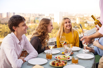 Cheerful friends drinking white wine during roof party