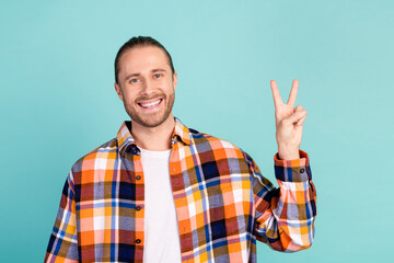 Naklejka premium Portrait of cheerful positive man with stubble wear flannel plaid jacket showing v-sign symbol isolated on turquoise color background