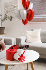 Glasses of wine with gifts for Valentine's Day on table in living room