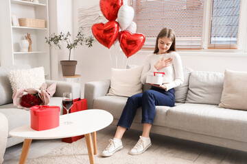Beautiful woman with gift box sitting at home on Valentine's Day