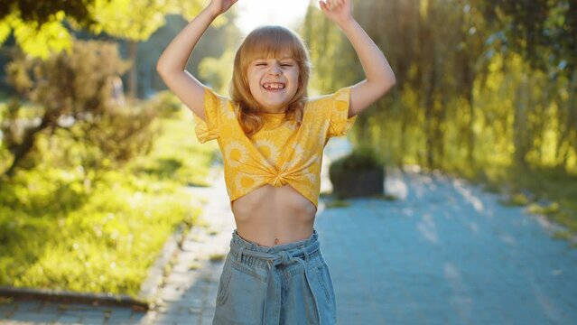 Preteen child kid shouting, celebrating success, winning, goal achievement, good news, lottery jackpot luck, victory, play game. Pretty blonde little girl standing on city sunset park street, outdoors