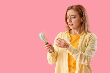Worried mature woman with hair loss problem and brush on pink background