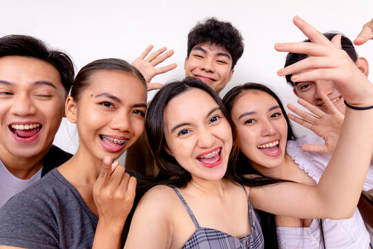 A cheerful group of six young friends smiling and posing for a selfie, or possibly saying hi to a friend via video call on a plain background.