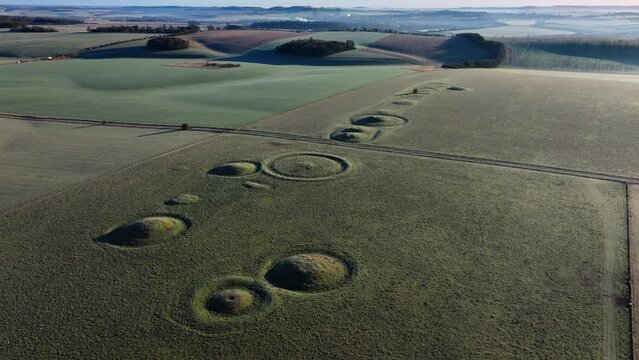 Aerial shot descending towards a series of ancient burial mounds and barrows in the English countryside near Stonehenge