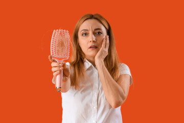 Worried mature woman with hair loss problem and brush on red background