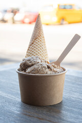 delicious pot of artisanal dulce leche ice cream with cone on wooden table on sunny day